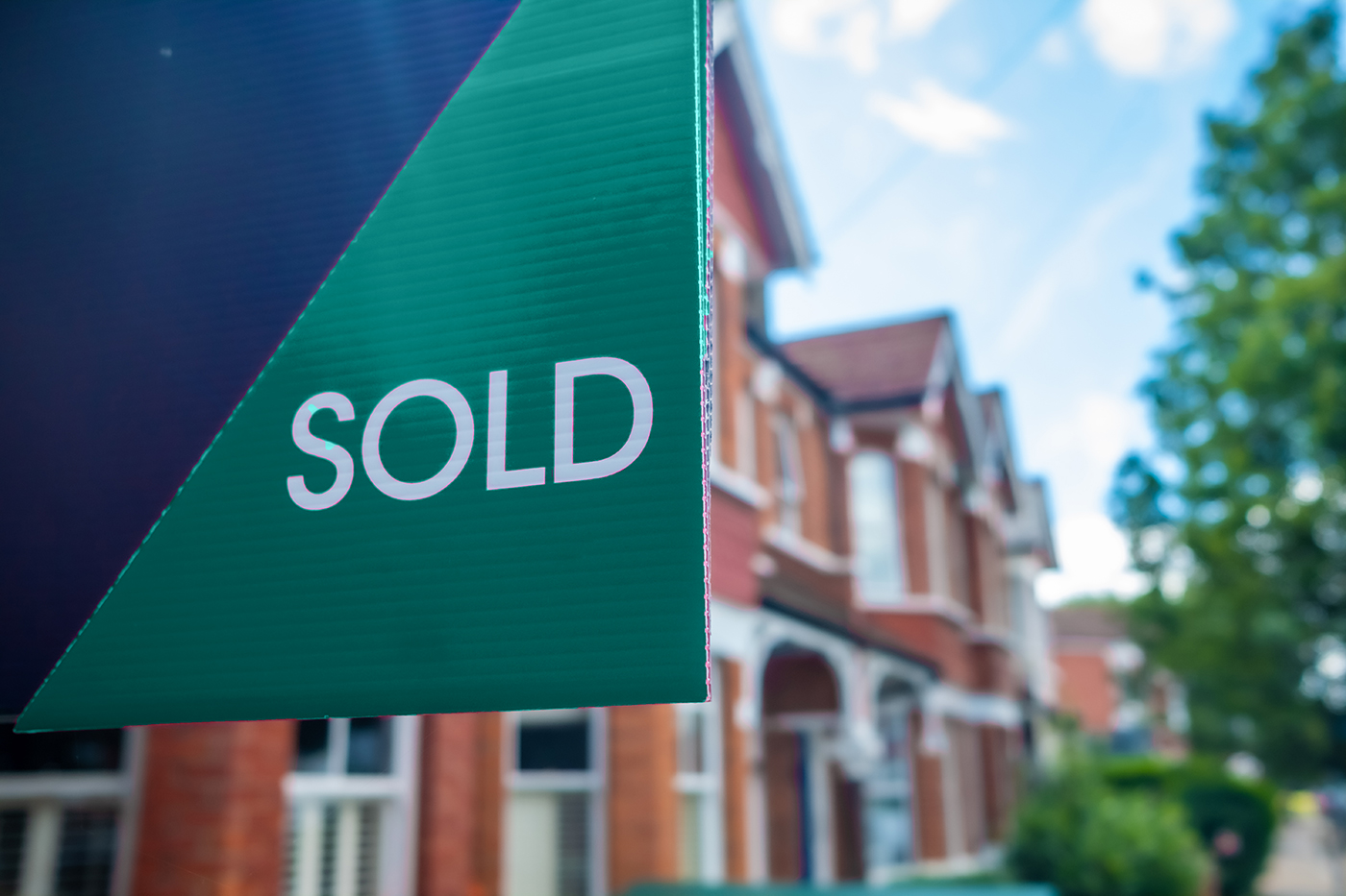 Russell-Cooke-Conveyancing fee information. Image of a for sale sign with a blurred background containing terraced houses.