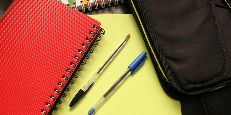 Red spiral bound notepad, blue and black biro pens on a yellow folder with a multi-coloured spiral-bound notepad and a bag. Disability discrimination — how schools can get it wrong
