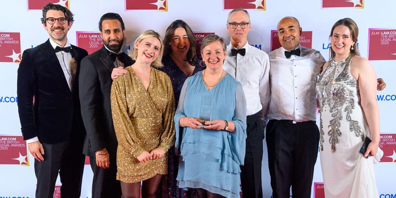 The picture shows a group of men and women smiling in black tie and dresses. 