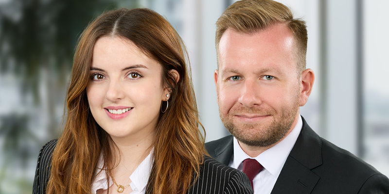 Brunette female in pin striped blazer. Male in the background with red tie and black blazer. Trainee solictors Sophie Lindsay and James Underwood.