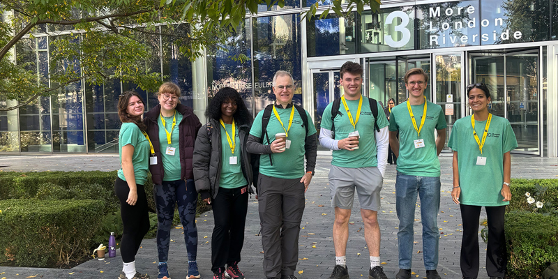 The picture shows a group of seven people stood under a tree in green tops and jackets.