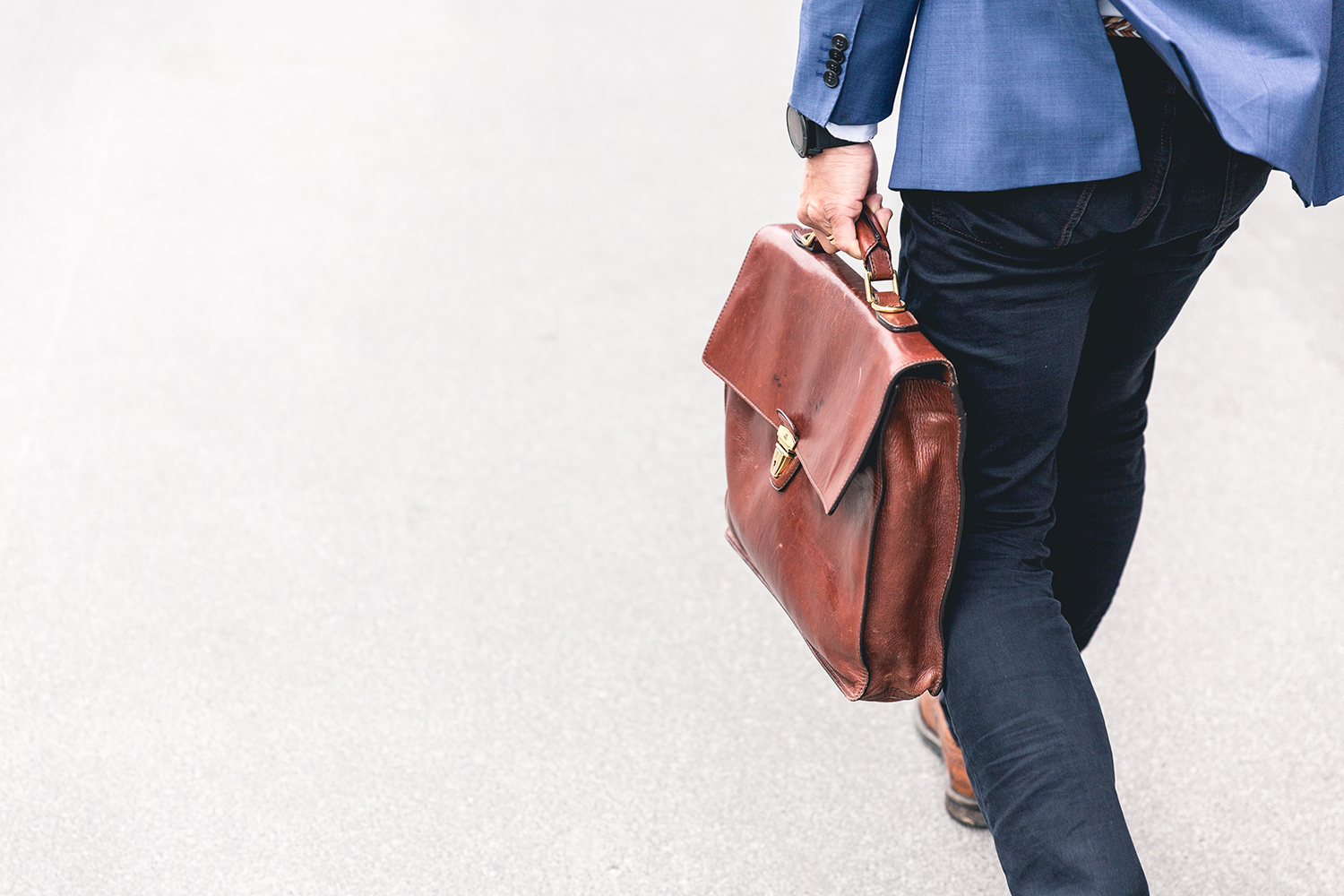 Russell-Cooke employment litigation charging information. Man walking and carrying a brown leather work bag. 