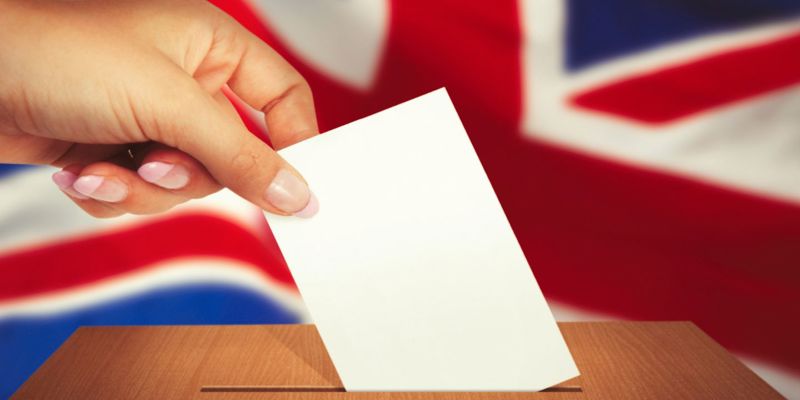 Hand putting voting card in ballot box in front of the United Kingdom flag. What does a Labour victory mean for corporate immigration?