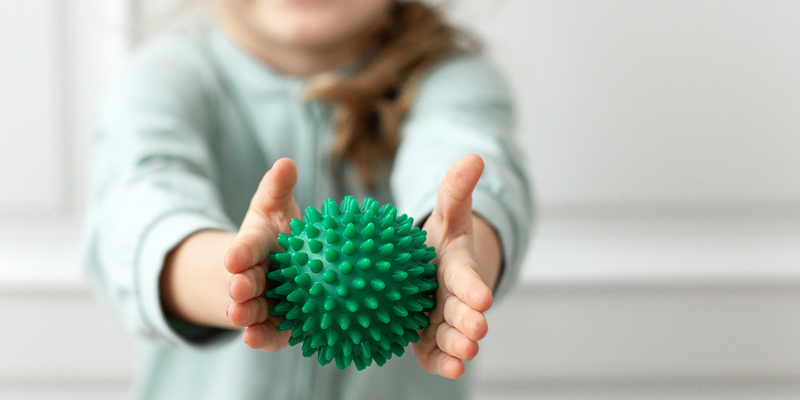 A young toddler holding green rubber physio ball in the foreground. Multi Trauma injury claims solicitors