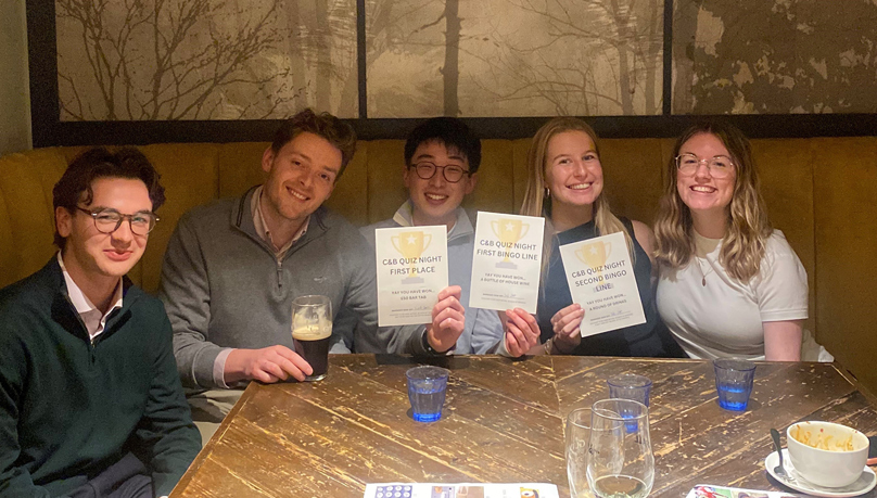A groupd of three men and two women sitting at a table, holding up a 'quiz winners' certificate. 