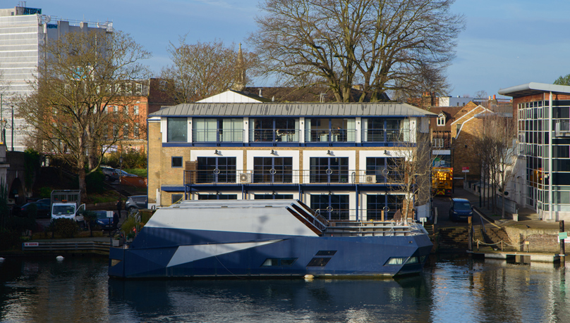 The picture shows a modern building with blue windows and verandas across from the River Thames