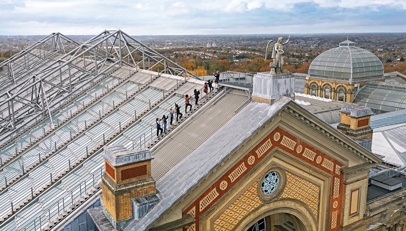 The picture shows a group of people participating in the Alexandra Palace rooftop summit climb experience - walking on the edge of the rooftop