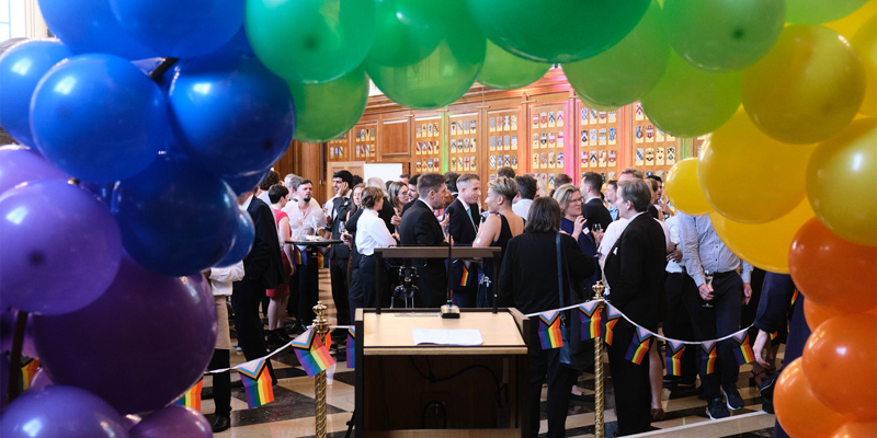 A rainbow arch of colourful balloons with event attendees networking in the background. Inner Temple – 'Pride in Practice'