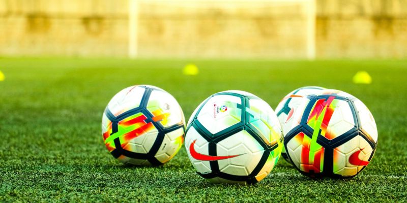 three footballs on the ground in front of a football pitch. News 07 June 2024 'Football’s coming home?'—Exploring the legal implications of football-related injuries in the lead up to Euro 2024