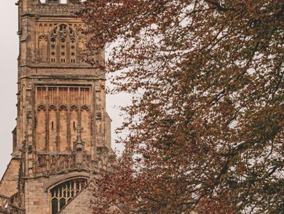  Tower of a historic stone church partially obscured by the autumnal branches of nearby trees.