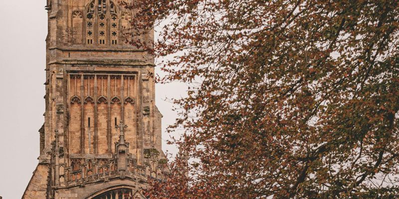 Tower of a historic stone church partially obscured by the autumnal branches of nearby trees.