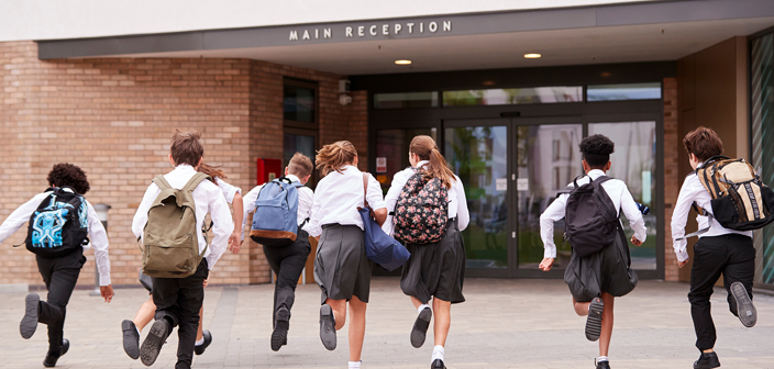 Eight school children running towards a school building. Disputes with independent and state funded schools
