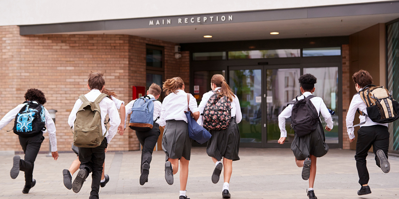 Eight school children running towards a school building. Disputes with independent and state funded schools