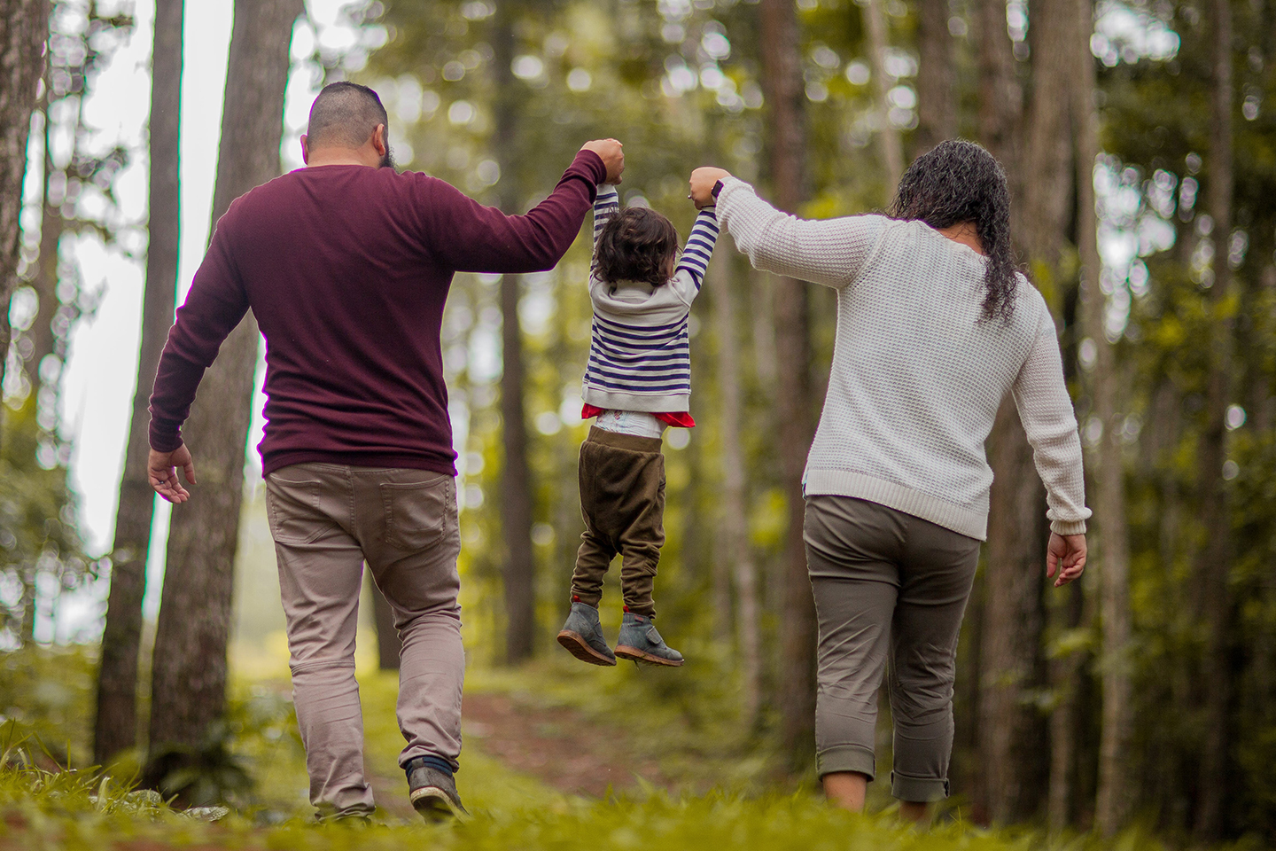 Man and Woman swinging child in the air playfully in an wooded area. The ‘one-stop shop’ for families—Family Hubs and Start for Life now open in local authorities across half the country