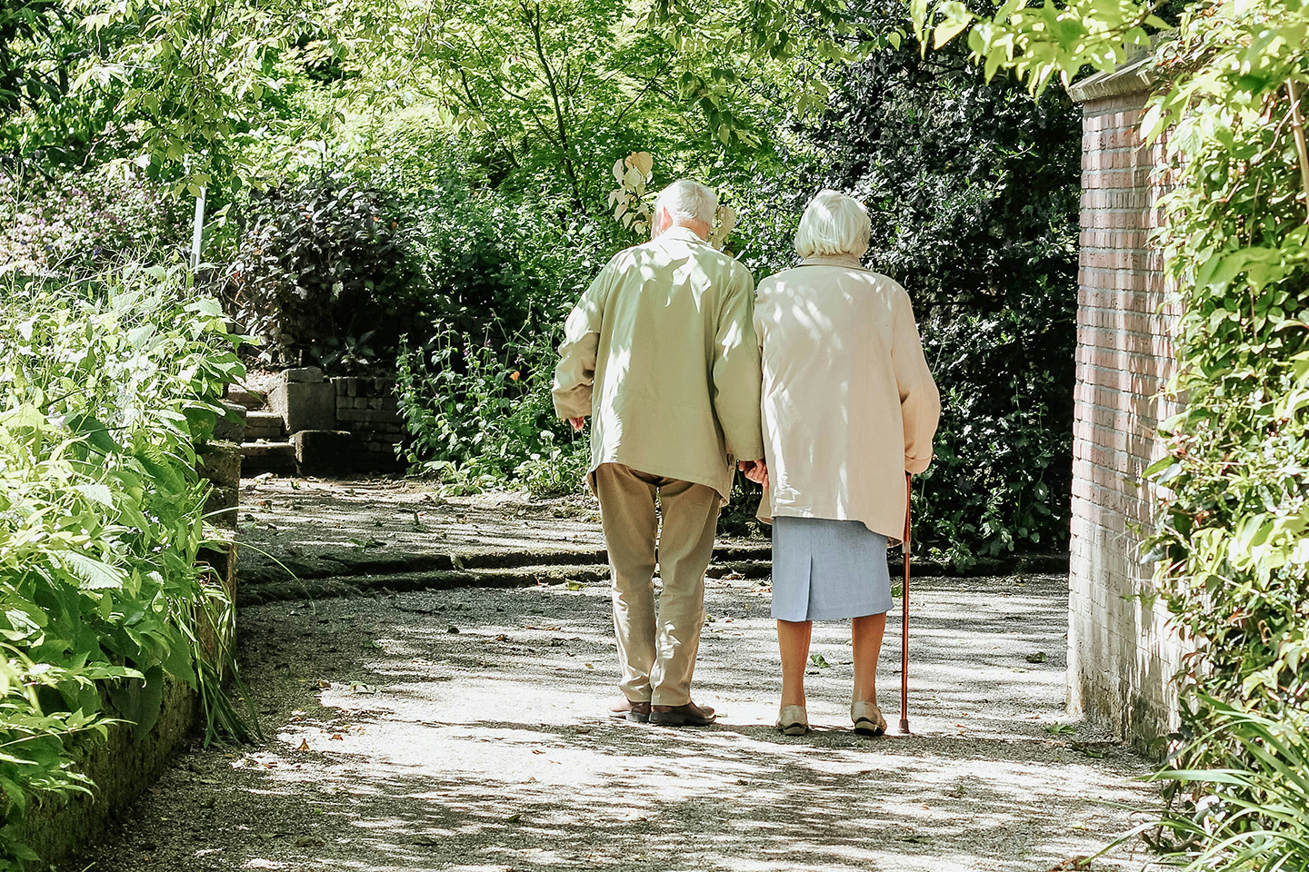 Elderly couple walking hand-in-hand in a leafy footpath. Lessons on immigration compliance for businesses–sponsor licence revoked for care home group
