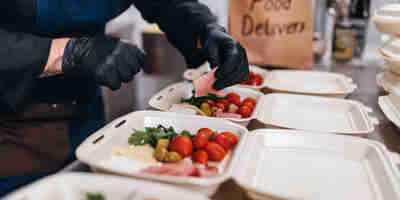 Russell-Cooke solicitors—What Are Dark kitchens? Image of a person preparing food into containers for food delivery