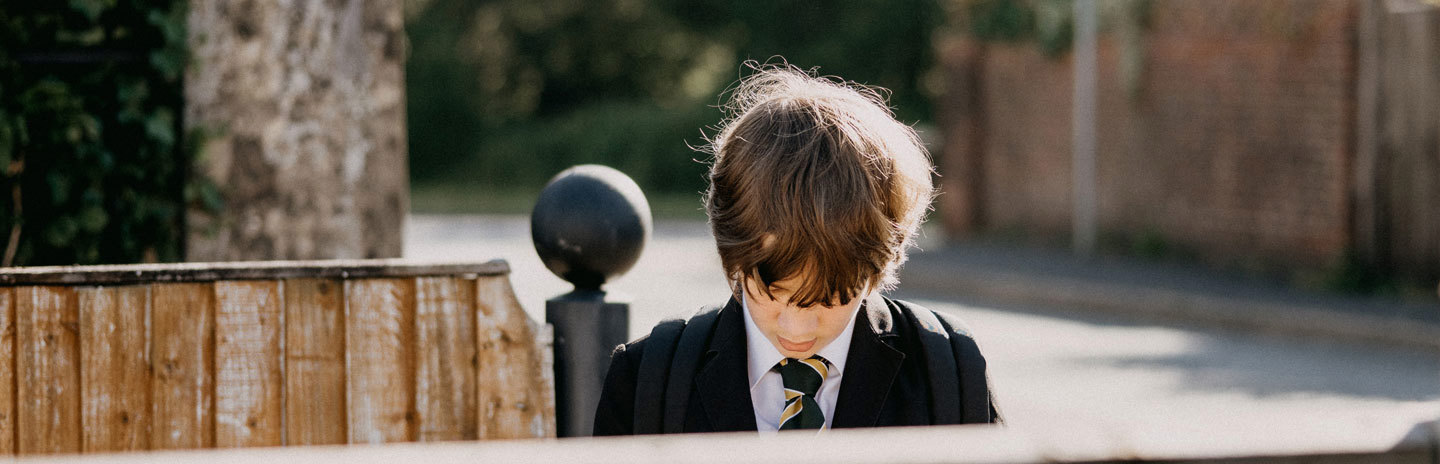 Russell-Cooke education law. An image of a school boy in uniform, stood behind a fence and looking down at the ground.