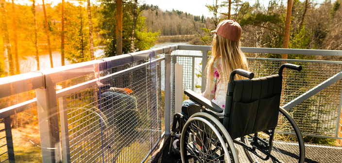 Young girl in a wheelchair on a balcony overlooking a river and tall trees. Spinal cord injury compensation claim solicitors