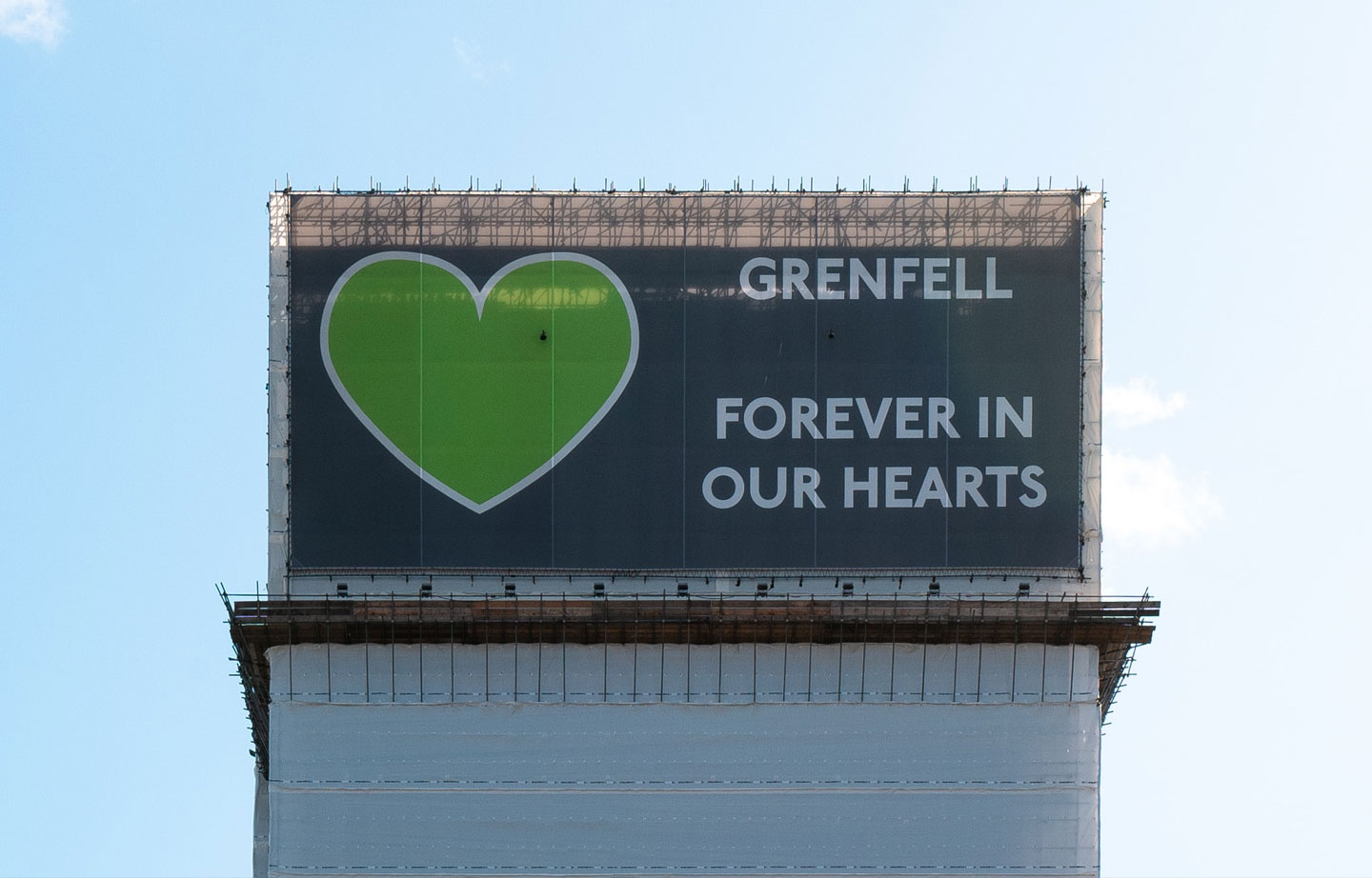 Image of a banner covering the Grenfell Tower. The banner has a large green heart and the words 