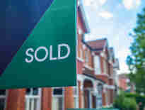 Russell-Cooke-Conveyancing fee information. Image of a for sale sign with a blurred background containing terraced houses.