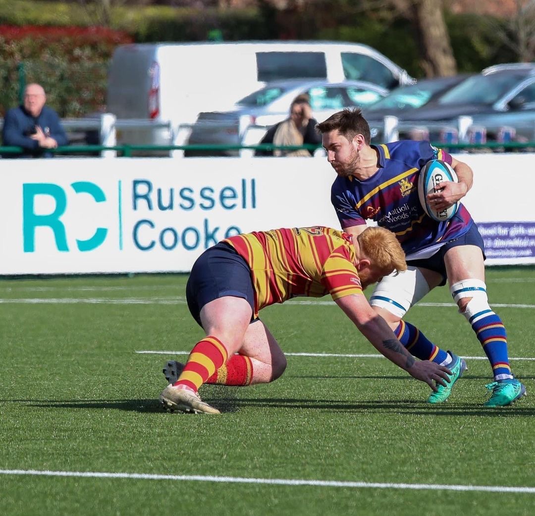 Action shot of wo opposing players from a Cobham RFC match Russell-Cooke sponsored banner in the background